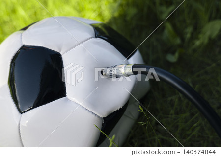 Inflating a soccer ball through a flexible hose with a needle, illustrating routine sports equipment maintenance and proper care. Inflating a soccer ball through a flexible hose with a needle, illustrating routine sports equipment maintenance and proper care. 140374044