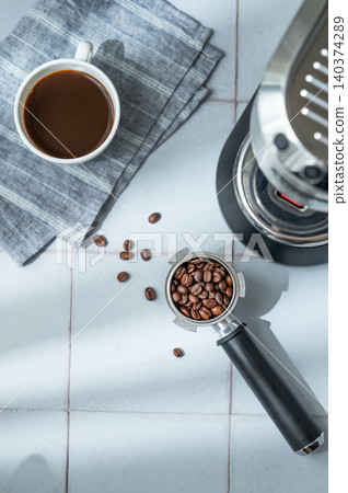 A flat lay of a cup of black coffee, a portafilter with roasted beans and an espresso machine A flat lay of a cup of black coffee, a portafilter with roasted beans and an espresso machine 140374289