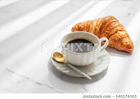 Freshly brewed black coffee in a cup on a white marble background with croissant Freshly brewed black coffee in a cup on a white marble background with croissant 140374303