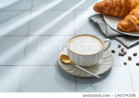 Freshly brewed cappuccino coffee in a cup on a blue tile background with croissants 140374306