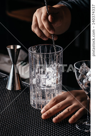 Bartender stirring cocktail in mixing glass with ice at bar counter close up Bartender stirring cocktail in mixing glass with ice at bar counter close up 140374337