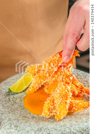 Hand picking crispy breaded shrimp with mango sauce and lime in gourmet seafood restaurant 140374434