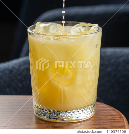 Fresh yellow citrus cocktail with ice cubes and falling splash in glass close up on dark background Fresh yellow citrus cocktail with ice cubes and falling splash in glass close up on dark background 140374506