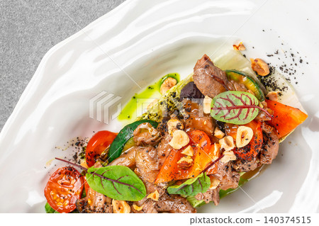 Gourmet meat salad with roasted vegetables hazelnuts and microgreens served on white plate Gourmet meat salad with roasted vegetables hazelnuts and microgreens served on white plate 140374515