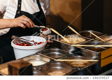 Preparing traditional Czech chimney cake dessert with strawberries and chocolate topping at street food stall 140374527