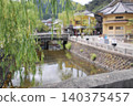 A picturesque scene of a river flowing through the charming Kinosaki Onsen town and a weeping willow standing in the foreground. 140375457