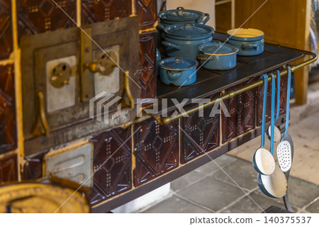 Rustic tiled stove displaying enamel cookware and kitchen utensils 140375537