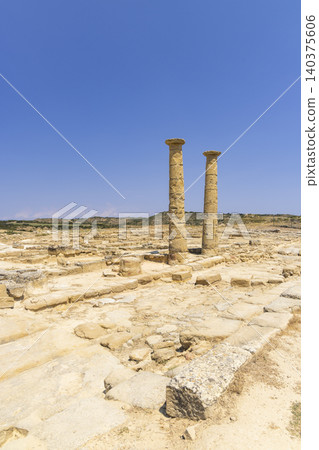 Two ancient Roman columns standing under a clear blue sky amidst ruins 140375606