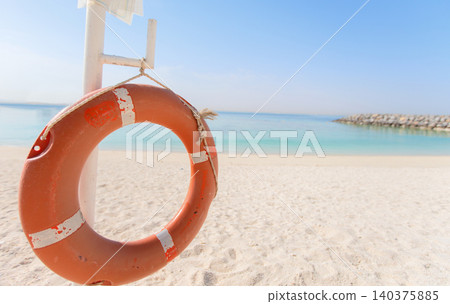 Life ring displayed on beach with clear blue water and gentle waves in bright sunlight during a peaceful afternoon Life ring displayed on beach with clear blue water and gentle waves in bright sunlight during a peaceful afternoon 140375885