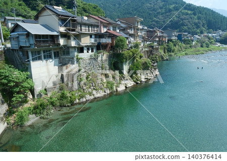 A mountain village landscape with houses lining the river. 140376414
