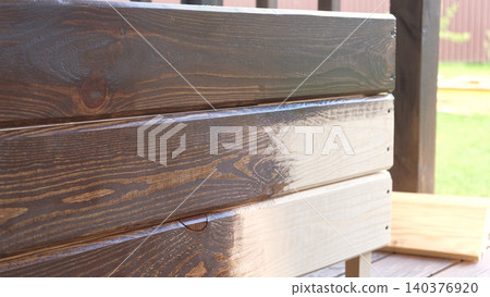 Brown oil for protection of wood by staining. Painting fence for protecting and pests. Woodworker applying finish to pine board box. Repairman varnishing with brush wooden fencing wall plank surface. 140376920