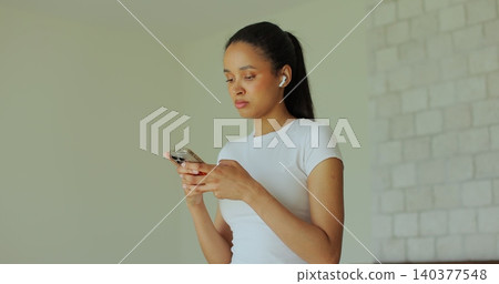 Sporty young american female in training clothes doing stepping exercises on running track and uses her smartphone. 140377548