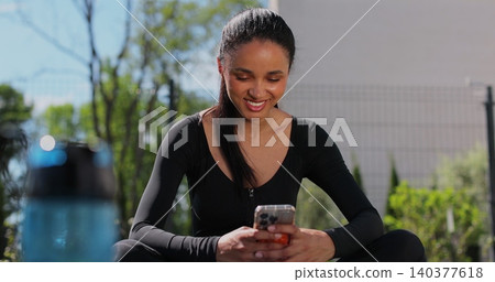 Young sport woman resting and using smartphone, after workout in backyard. Mobile application for training. Sports female doing outdoor training. Young sport woman resting and using smartphone, after workout in backyard. Mobile application for training. Sports female doing outdoor training. 140377618