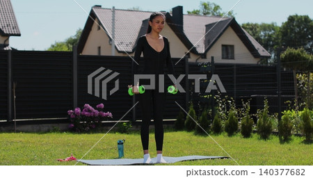 Young beautiful sports girl in leggings does exercises with dumbbells. Healthy lifestyle. Woman goes in for sports outdoor at home. 140377682