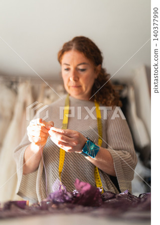 Female craftswoman designer tailor working with fabric and thread, measuring tape draped around her neck, surrounded by colorful materials in a well-lit studio Female craftswoman designer tailor working with fabric and thread, measuring tape draped around her neck, surrounded by colorful materials in a well-lit studio 140377990