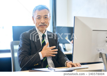 A senior businessman speaking with his hand on his chest in the office. 140378004