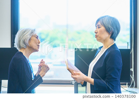 Senior women discussing documents in a conference room. 140378100