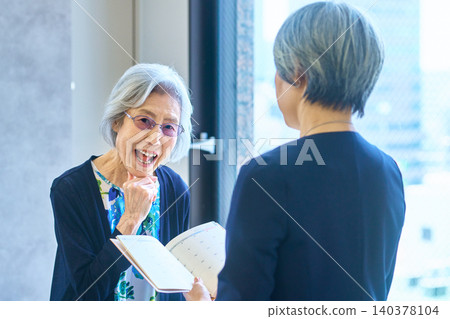 一位面帶微笑的老婦人一邊展示文件一邊講話。 一位面帶微笑的老婦人一邊展示文件一邊講話。 140378104
