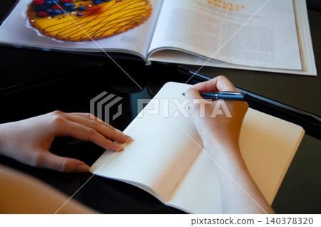 一位女士正在筆記本上做筆記,她的雙手在動。 一位女士正在筆記本上做筆記,她的雙手在動。 140378320