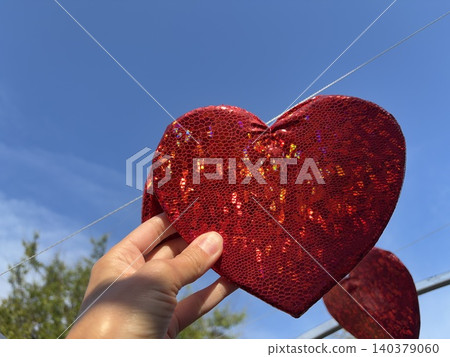 a hand holding a large, shimmering red heart against a vibrant blue sky. a hand holding a large, shimmering red heart against a vibrant blue sky. 140379060