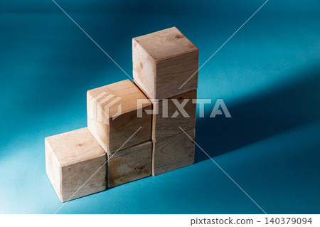 Wooden blocks stacked to form an ascending staircase shape against a cyan blue background, highlighting the concept of step-by-step progress, improvement, and corporate success. Wooden blocks stacked to form an ascending staircase shape against a cyan blue background, highlighting the concept of step-by-step progress, improvement, and corporate success. 140379094