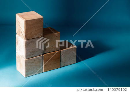 Six wooden cubes stacked in a step or staircase formation against a deep blue background with sharp lighting and long shadows, conceptualizing career advancement or financial growth. Six wooden cubes stacked in a step or staircase formation against a deep blue background with sharp lighting and long shadows, conceptualizing career advancement or financial growth. 140379102