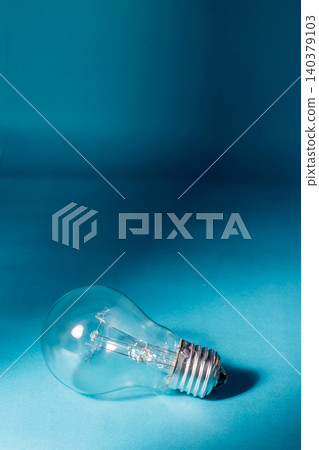 A traditional clear glass light bulb lying on its side over a turquoise blue background, illuminated with strong spot light, representing a bright idea, innovation, or creativity. A traditional clear glass light bulb lying on its side over a turquoise blue background, illuminated with strong spot light, representing a bright idea, innovation, or creativity. 140379103