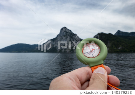 Hand holding a portable over Lake Traunsee with the Austrian Alps in the background, presenting a compact outdoor exploration tool Hand holding a portable over Lake Traunsee with the Austrian Alps in the background, presenting a compact outdoor exploration tool 140379238