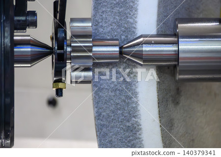 Close-up of the surface finishing process on metal shaft parts using a cylindrical grinding machine with an abrasive wheel. 140379341