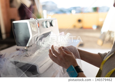 Sewing fabric with a sewing machine in a workspace during daylight hours Sewing fabric with a sewing machine in a workspace during daylight hours 140379462