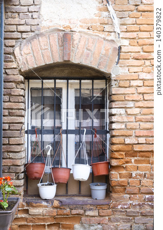 A window with bars is decorated with several hanging flower pots A window with bars is decorated with several hanging flower pots 140379822