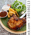 Grilled Pork Chop Steak on Banana Leaf Wooden Plate with French Fries Fresh Salad and Sauces 140380213