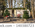 Cozy retro camper trailer decorated for Christmas with pine trees and outdoor furniture in a sunny winter forest. 140380723