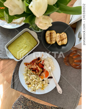 A table is set with a plate of rice, baked vegetables, fresh salad, broccoli pie, and baked apples for dessert. Enjoy healthy meals at home any time of day 140380832