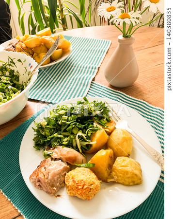 A delicious meal featuring baked rabbit and golden roasted potatoes is served on a round, ridged plate. Accompanying the dish is a glass of water with lemon slices, a small bowl of ketchup A delicious meal featuring baked rabbit and golden roasted potatoes is served on a round, ridged plate. Accompanying the dish is a glass of water with lemon slices, a small bowl of ketchup 140380835