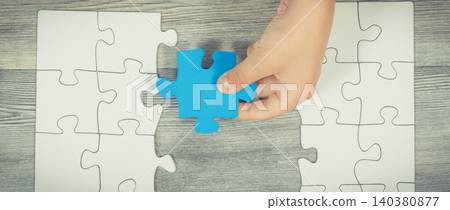 Hand of child putting together white and blue puzzle Hand of child putting together white and blue puzzle 140380877