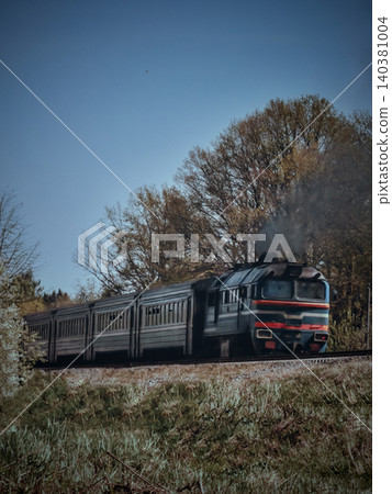 Passenger train traveling along a rural track beside autumn trees Passenger train traveling along a rural track beside autumn trees 140381004