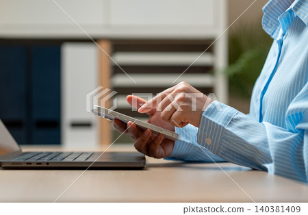 Side view close up hands of woman hold mobile phone over laptop and use the index finger to point or touch to screen of mobile phone in concept of modern business communication. Side view close up hands of woman hold mobile phone over laptop and use the index finger to point or touch to screen of mobile phone in concept of modern business communication. 140381409