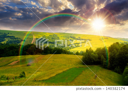 sunset over rural fields near pikui mountain in summertime. beautiful view of agricultural area. gorgeous mountain ridge with haystack on a grassy pasture. summer scenery. weather with rainbow sunset over rural fields near pikui mountain in summertime. beautiful view of agricultural area. gorgeous mountain ridge with haystack on a grassy pasture. summer scenery. weather with rainbow 140382174