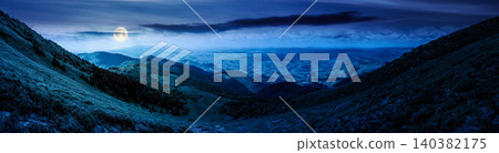 beautiful panorama of mountainous landscape at night. full moon over wide view of cloudy sky over the grassy slope of a mountain ridge. mysterious summer weather. adventure tourism in highland 140382175
