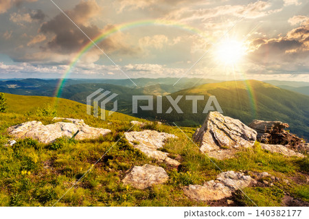 sunset over Carpathian mountain summer landscape. meadow with huge stones among the grass on top of the hillside near the peak of mountain range. alpine meadow and rolling hills. weather with rainbow sunset over Carpathian mountain summer landscape. meadow with huge stones among the grass on top of the hillside near the peak of mountain range. alpine meadow and rolling hills. weather with rainbow 140382177
