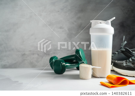 Protein shake and whey powder with dumbbells and running shoes, fitness nutrition concept, copy space Protein shake and whey powder with dumbbells and running shoes, fitness nutrition concept, copy space 140382611