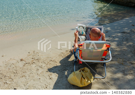 rear view of a Man Reading Newspaper in Beach Chair on Sunny Tropical Shore rear view of a Man Reading Newspaper in Beach Chair on Sunny Tropical Shore 140382880