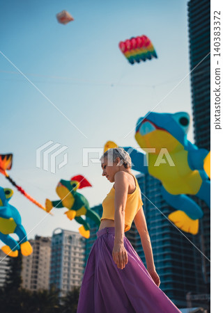 young woman walking on sand beach at colorful kite toys festival during summer sunset, girl enjoying freedom and joy at outdoor event by sea young woman walking on sand beach at colorful kite toys festival during summer sunset, girl enjoying freedom and joy at outdoor event by sea 140383372