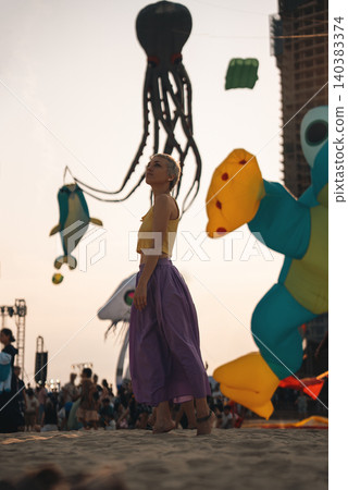 young woman walking on sand beach at colorful kite toys festival during summer sunset, girl enjoying freedom and joy at outdoor event by sea young woman walking on sand beach at colorful kite toys festival during summer sunset, girl enjoying freedom and joy at outdoor event by sea 140383374