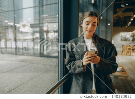 Smiling young Caucasian woman in her twenties texting on smartphone inside a modern cafe 140383952