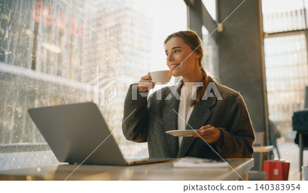 Smiling young adult Caucasian woman drinking coffee with laptop in modern cafe Smiling young adult Caucasian woman drinking coffee with laptop in modern cafe 140383954