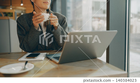 Caucasian young adult woman holding coffee cup while working on laptop inside modern cafe Caucasian young adult woman holding coffee cup while working on laptop inside modern cafe 140384023