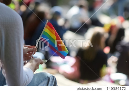 Hand holding rainbow pride flag during outdoor lgbtq community gathering Hand holding rainbow pride flag during outdoor lgbtq community gathering 140384172