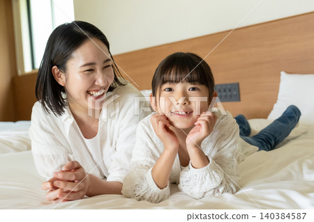 A parent and child lying on a bed 140384587